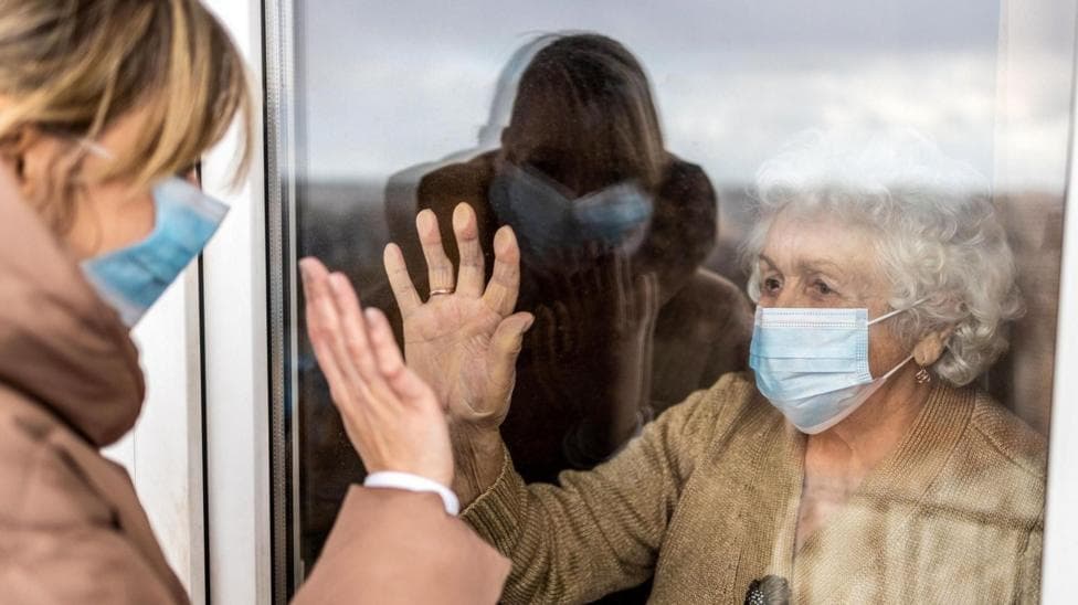 Care home resident looking through window to family member