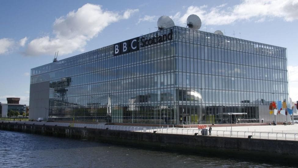 A large square windowed building with a large sign saying 'BBC Scotland' it. It has antennas coming from the top.