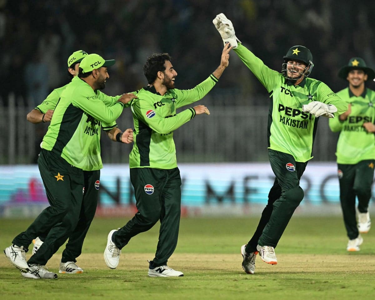 Pakistan cricketers celebrate a wicket, high-fiving as they run across the pitch