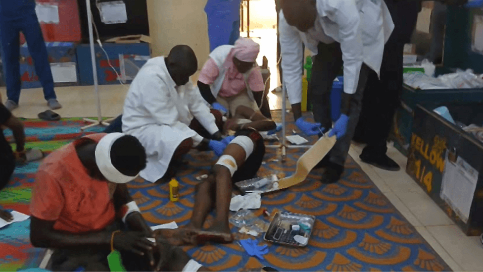 Medical workers - two men in white coats and a nurse in a pink uniform - treat injured people at Ameth Bek Hospital on the floor after a drone strike on a market in the disputed Abyei region along the border between South Sudan and Sudan, 19 October 2026.