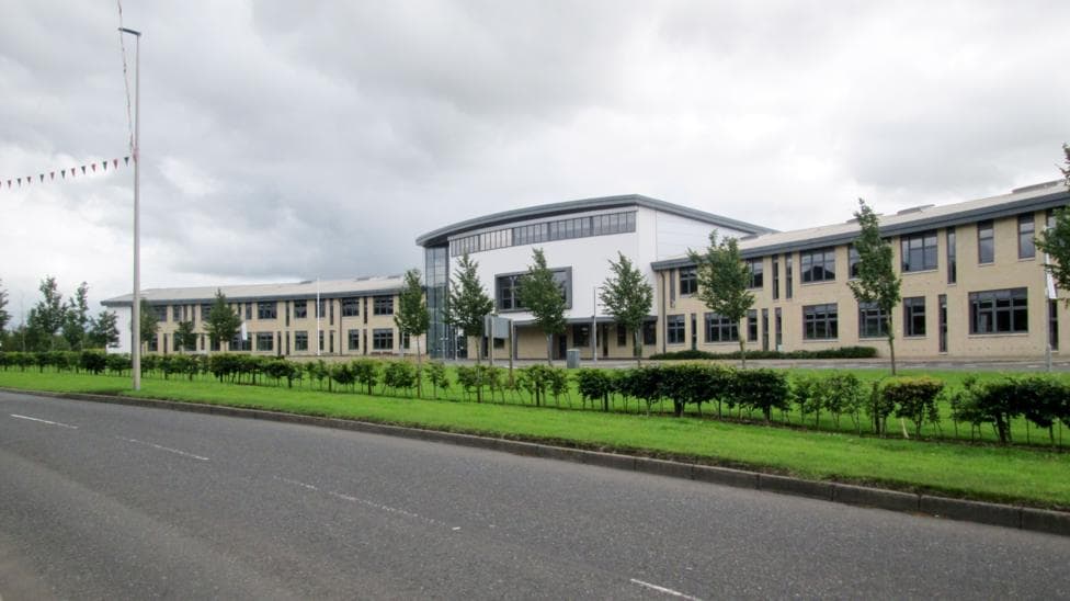 The Berwickshire High School building, a modern structure with white front and and trees and a lawn and road in front