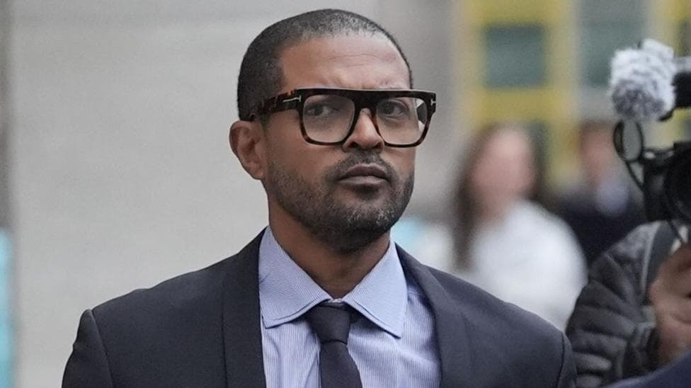 Noel Clarke arriving at court in a grey suit and tie and glasses