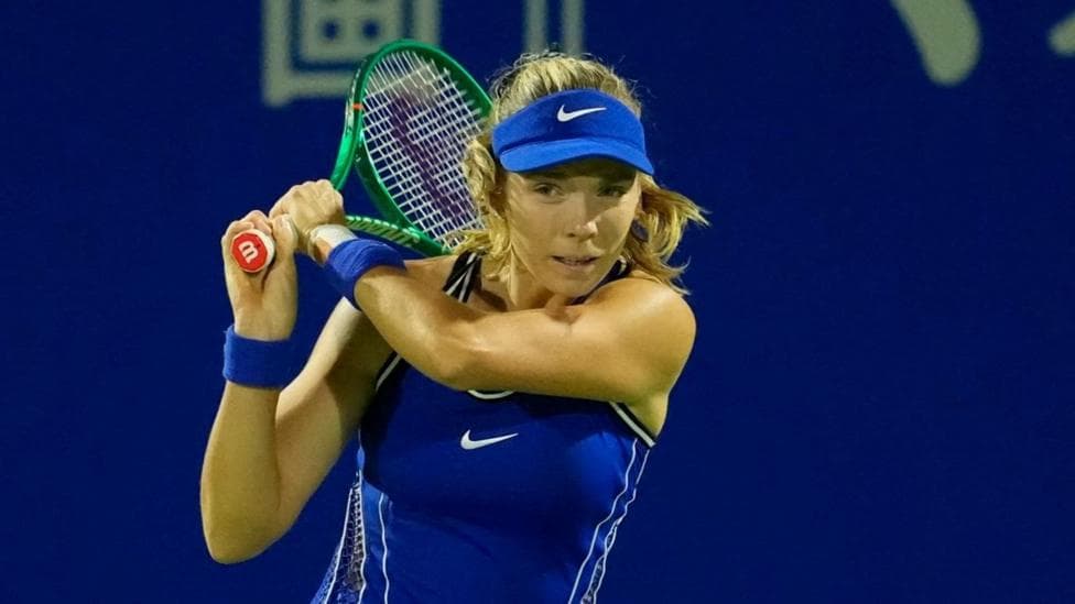 Katie Boulter in a blue outfit and cap, with her racket held near her head after playing a shot