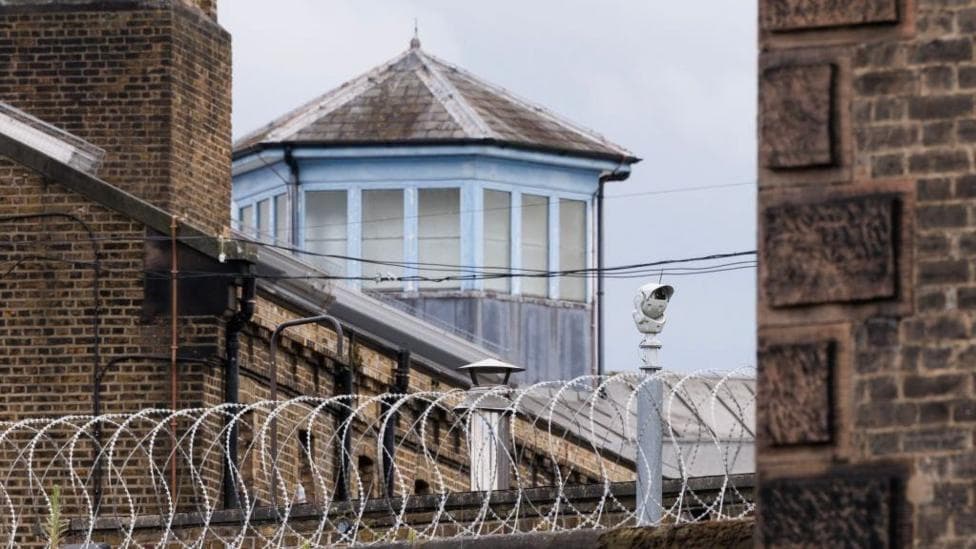 Barbed-wired fencing above brown brick walls with a security cameras are pictured at the HMP Wandsworth prison in London, England.
