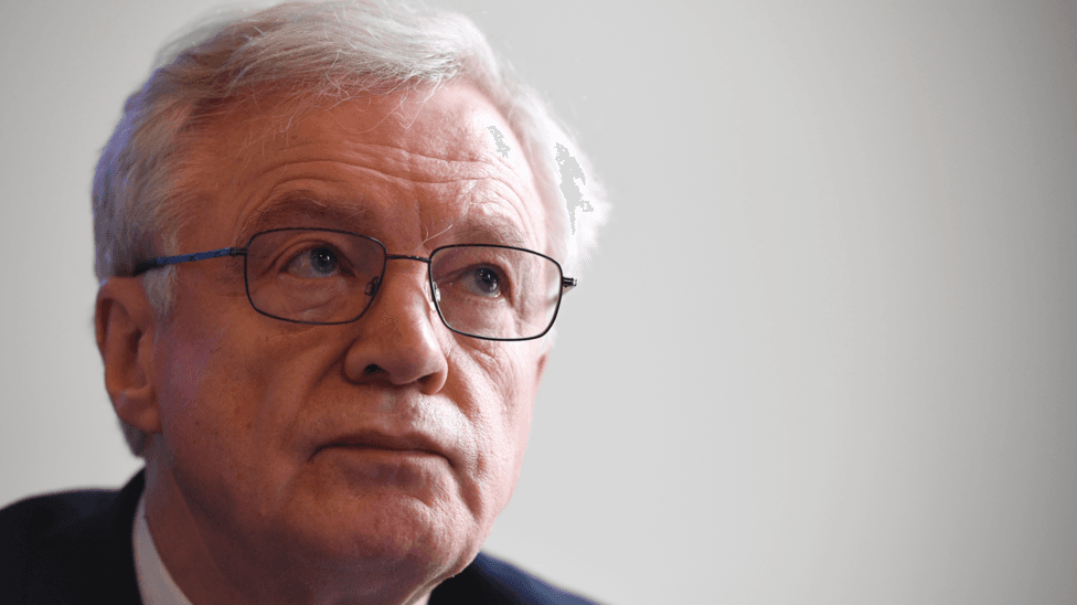 A close up of Sir David Davis. He us wearing glasses and a suit with a white shirt.