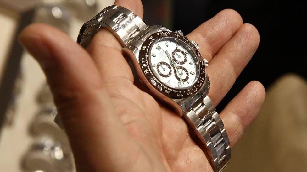 A person's hand is seen holding a Rolex watch