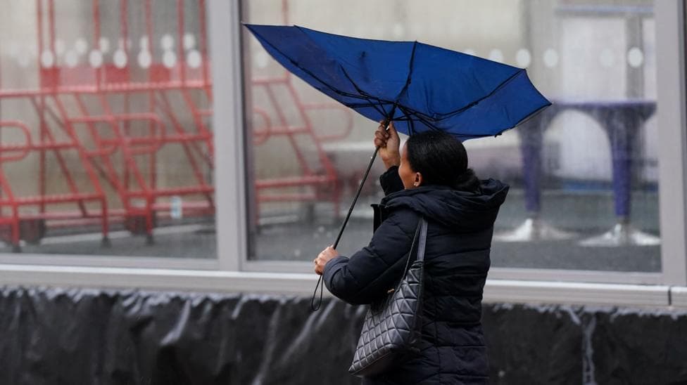 A woman is attempting to control her umbrella which has folded inside out because of strong winds.