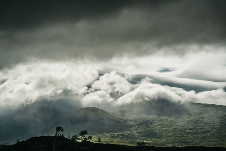 A dramatic scene of clouds rolling over the lush green mountains of Glencoe, Scotland.