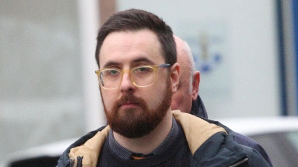 A 36-year-old man with a beard and glasses, wearing a jacket, pictured outside