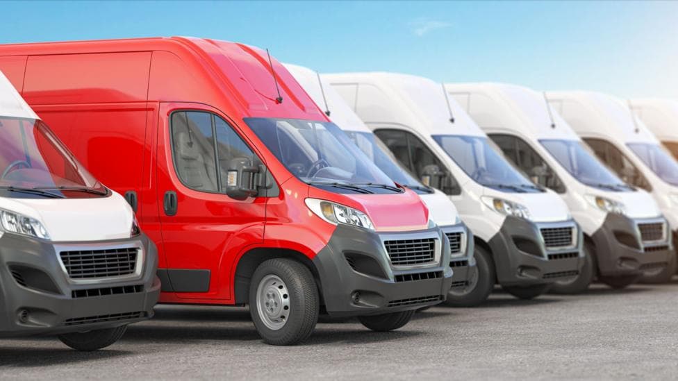 A red van among a line up of white vans.
