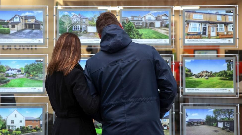 A couple look at houses for sale in the window of an estate agent