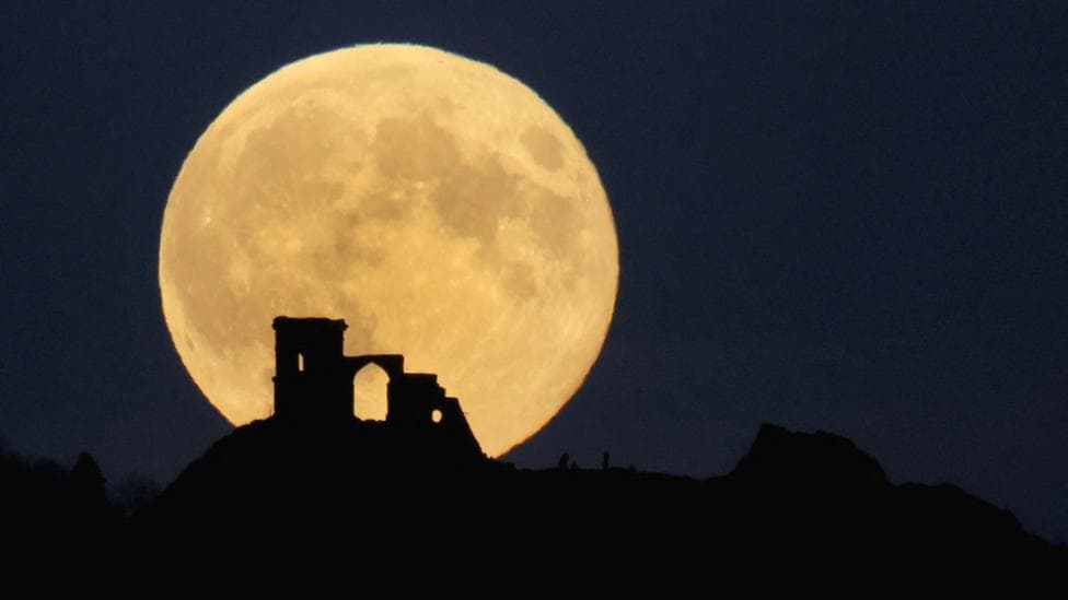 Large, full supermoon with a yellowy tint rises behind the silhouette of a ruined castle