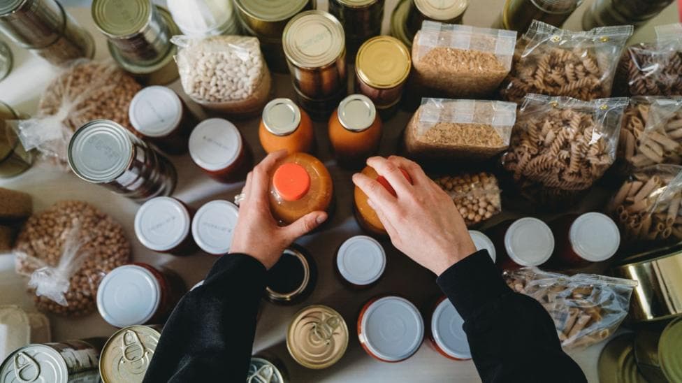 Woman is rearranging the kitchen pantry. Many cans, bottles and tins on the kitchen table. Panic buying concept.