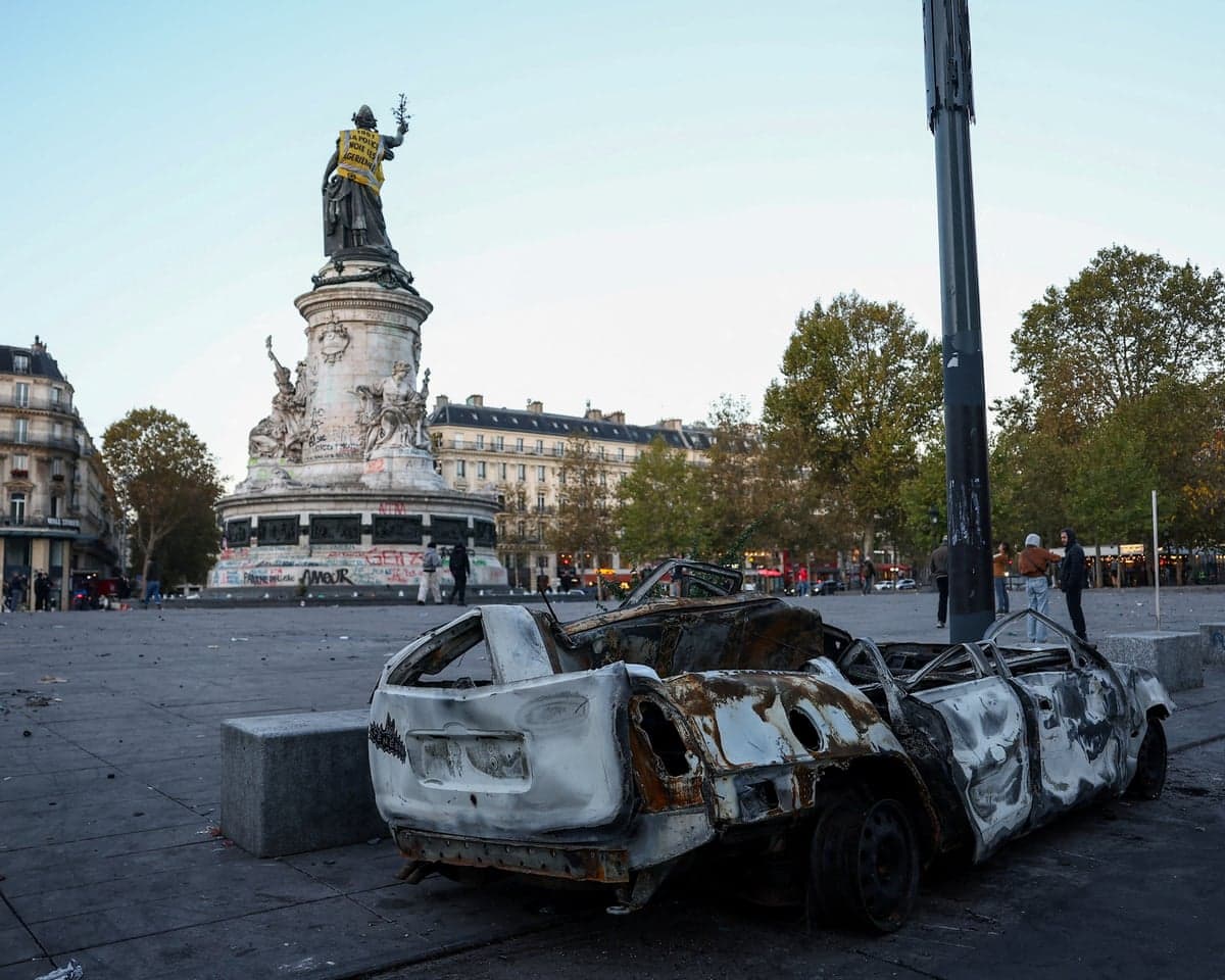 A burnt-out car near the Marianne statue at the Place de la Republique, with a yellow vest put on it