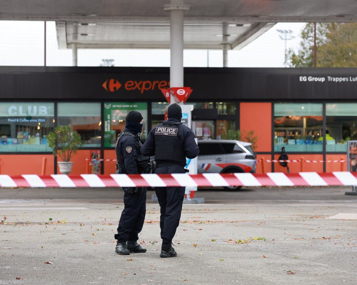 Armed, masked police stand behind cordon tape at a shooting scene in Trappes, France