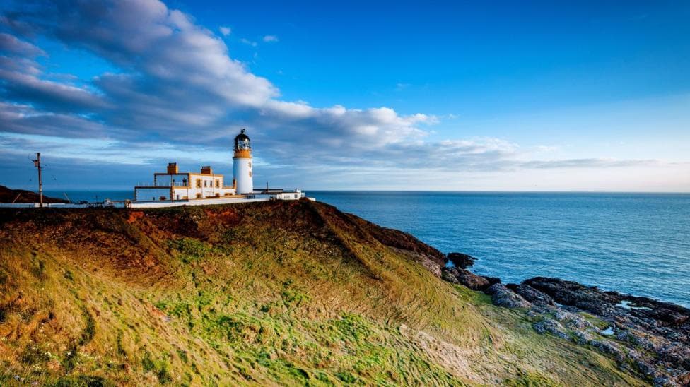 A view of a lighthouse on the Galloway coast in bright white and yellow with a view out over the water