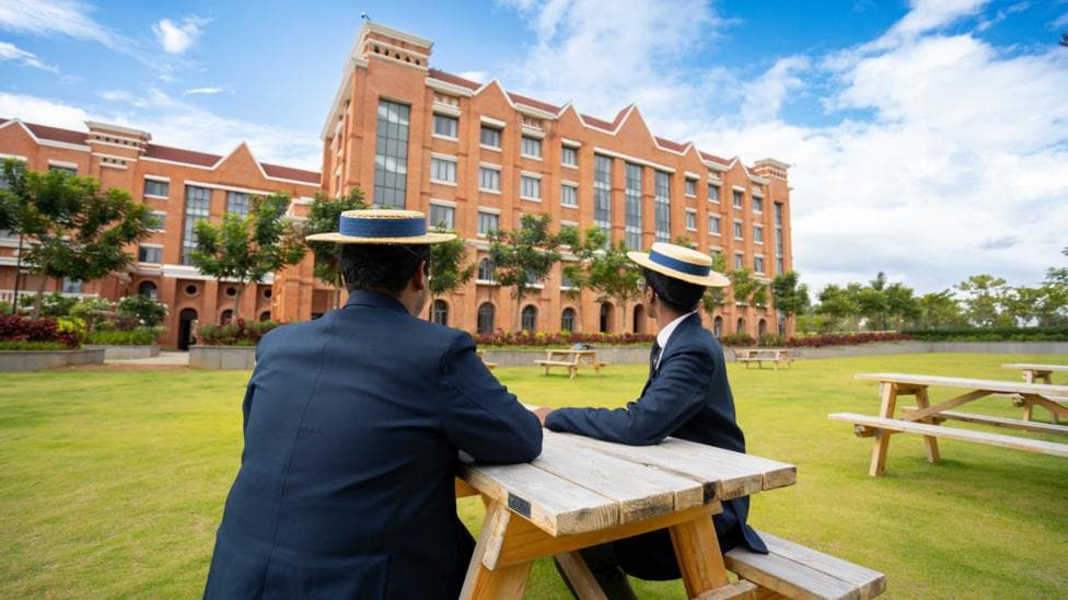 Harrow school, Bengaluru students sitting in the garden and looking at the main building wearing traditional uniforms and hats.