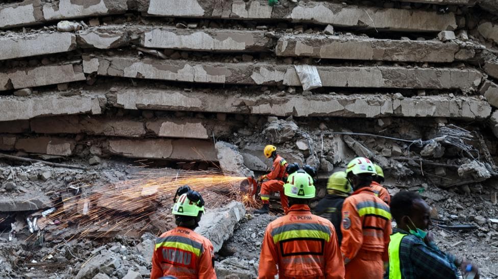 An emergency worker saws through metal and concrete as others watch on at the site of a building collapse in Nairobi.