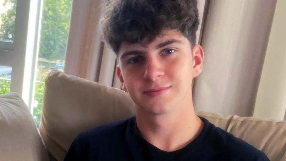 Head and shoulders shot of student Eddie Lever in a black T shirt, sitting on a sofa in a living room