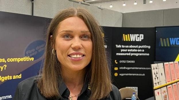 Michelle Bunker in a black shirt with trade signs behind her and an oversized card game on the right