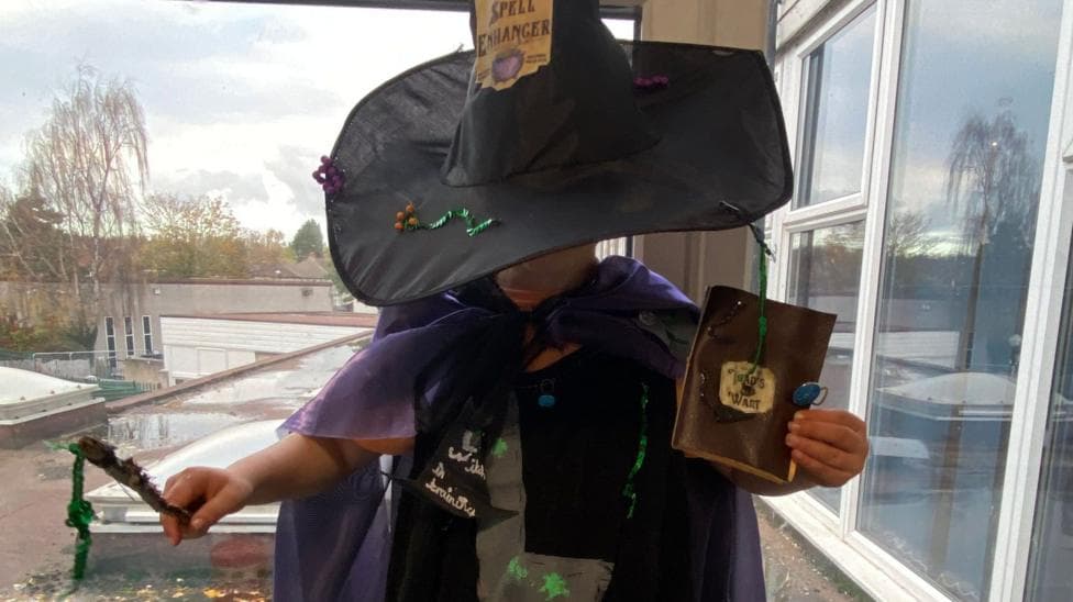 Child dressed as a witch in a homemade Halloween costume featuring a black hat, purple cape, wand and handmade accessories.