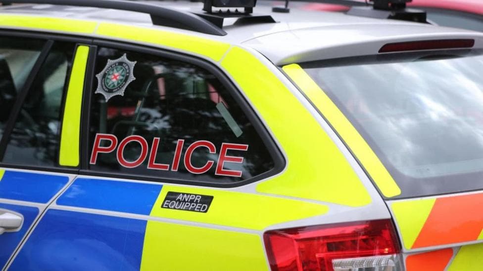 A blue and yellow PSNI car with the word police on the window.