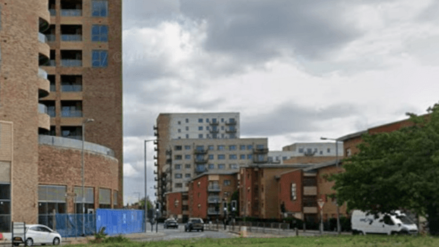 St Paul's Road, near a grass covered roundabout. There are several high rise buildings on both sides of the road, which are in red and brown brick. Cars and a van are seen travelling in and out of the road.