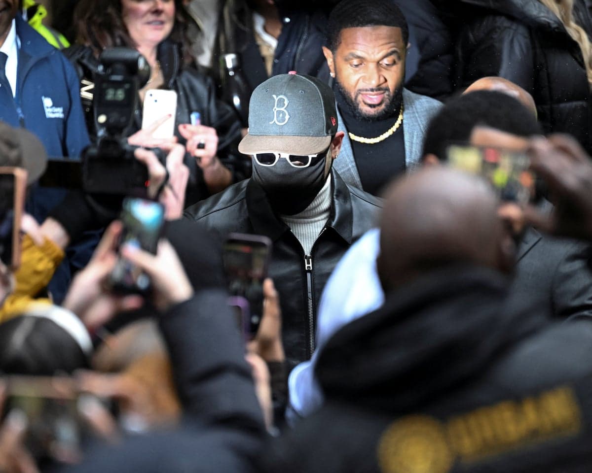 Chris Brown, wearing sunglasses and a face mask, walks through a crowd of photographers outside court
