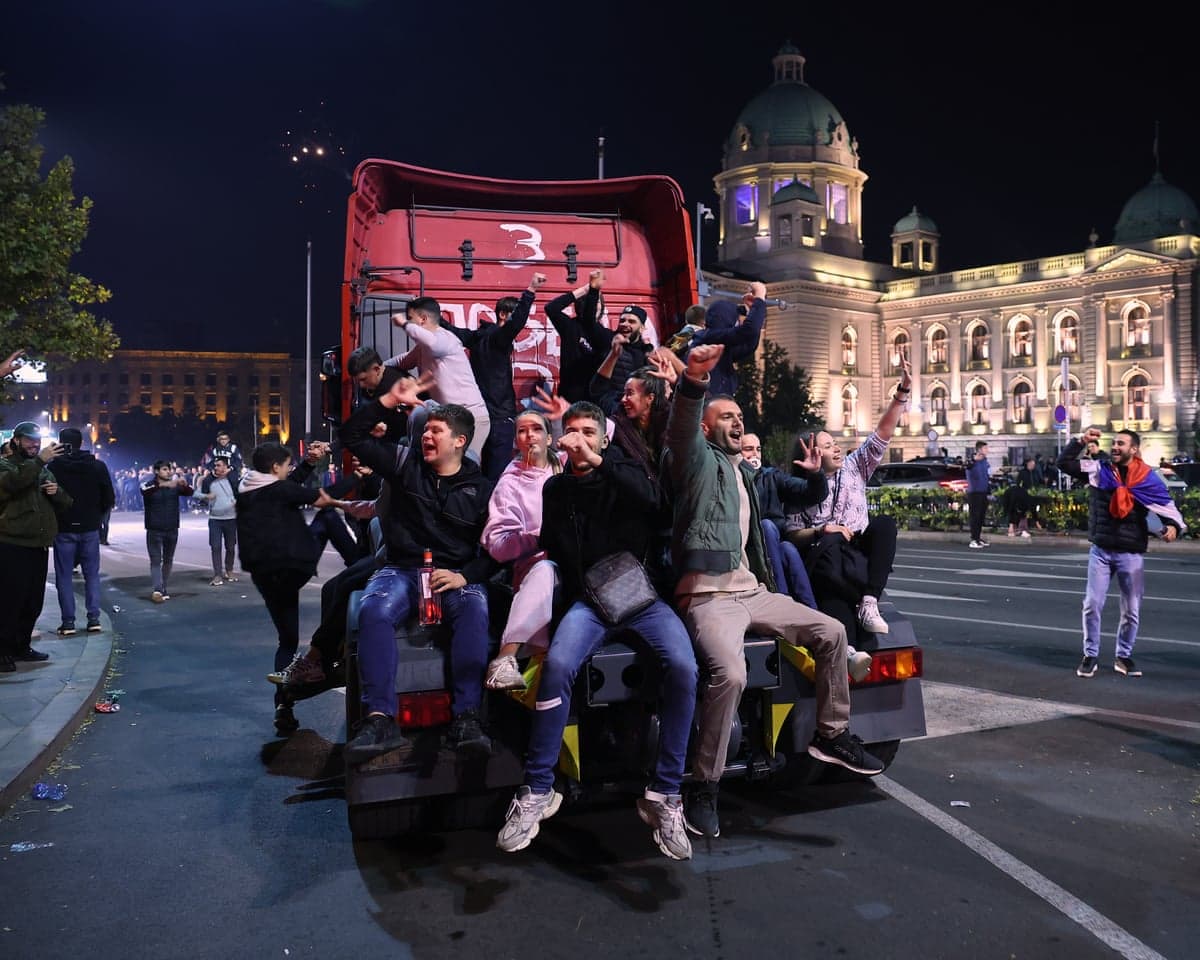 Young adults raise their fists on the back of an articulated lorry cab on a city street