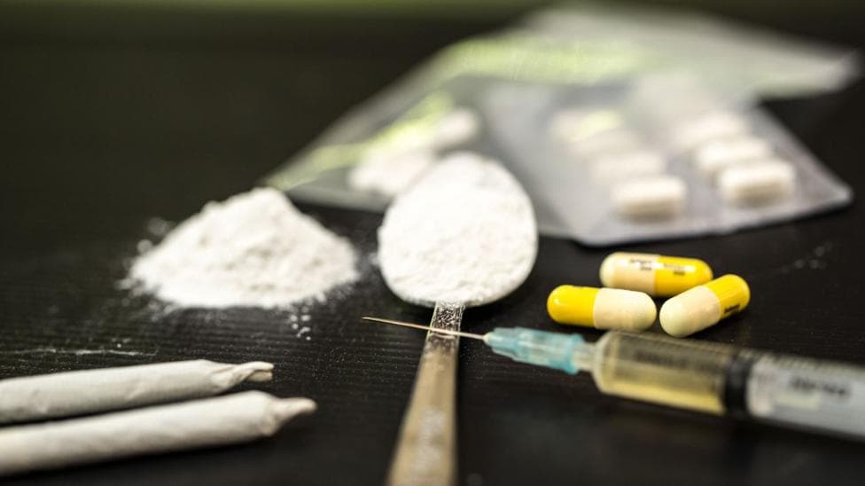 A spoon, pile of white powder, syringe, and pills on a flat surface.