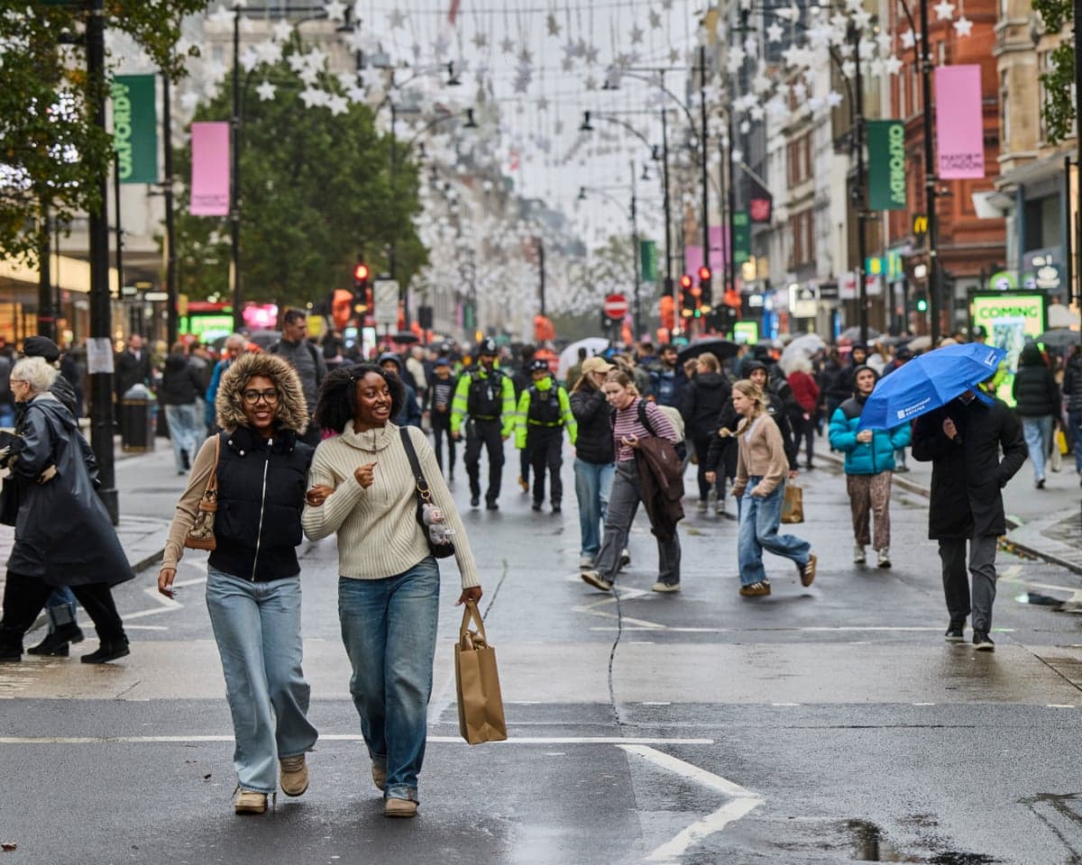 Two smiling women walk arm in arm along pedestrianised Oxford Street, decorated with hanging star lights