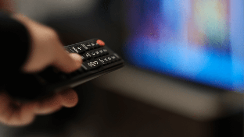 Remote control in a hand is changing channels.