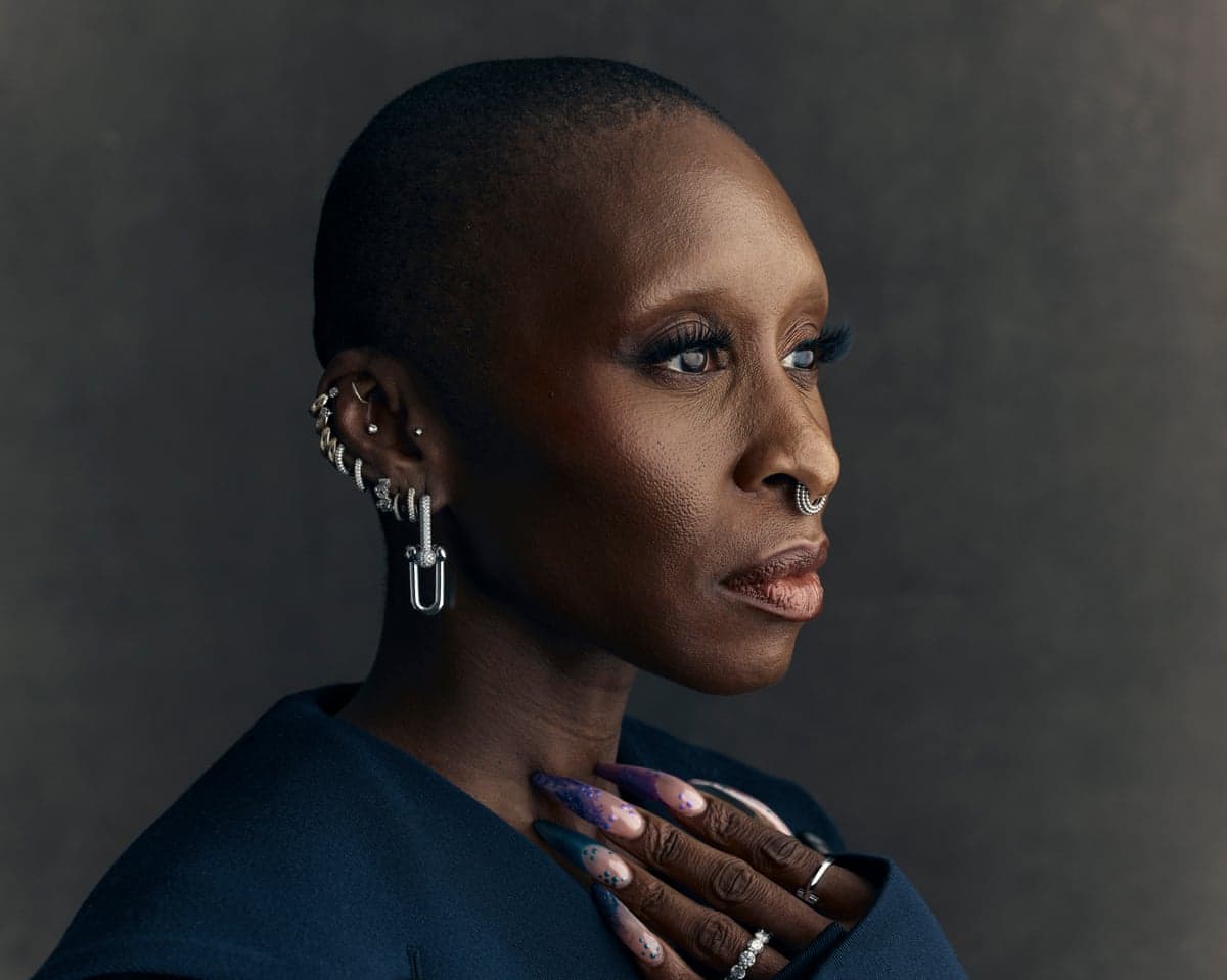 A closeup of Cynthia Erivo with shaved head , decorated nails and wearing metal nose rings and earrings
