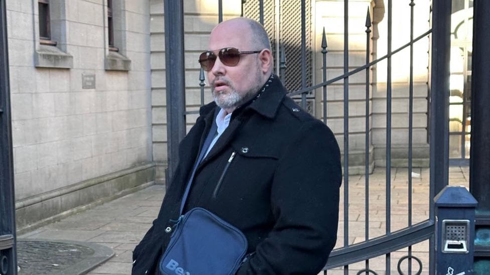 Joseph Hedley leaving Edinburgh Sheriff Court. He is bald and is wearing sunglasses and a long, black coat. He has a small shoulder bag over his left shoulder.