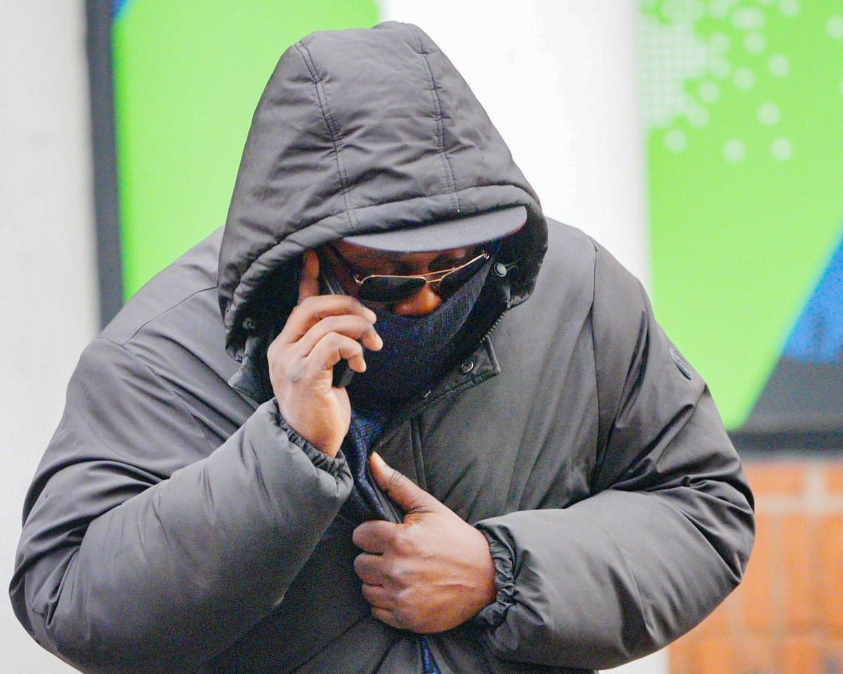 Man in sunglasses with hood up speaking on phone as he arrives at court.