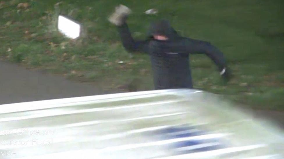 Kieran Sutherland wearing all black throwing a brick at a police van.
