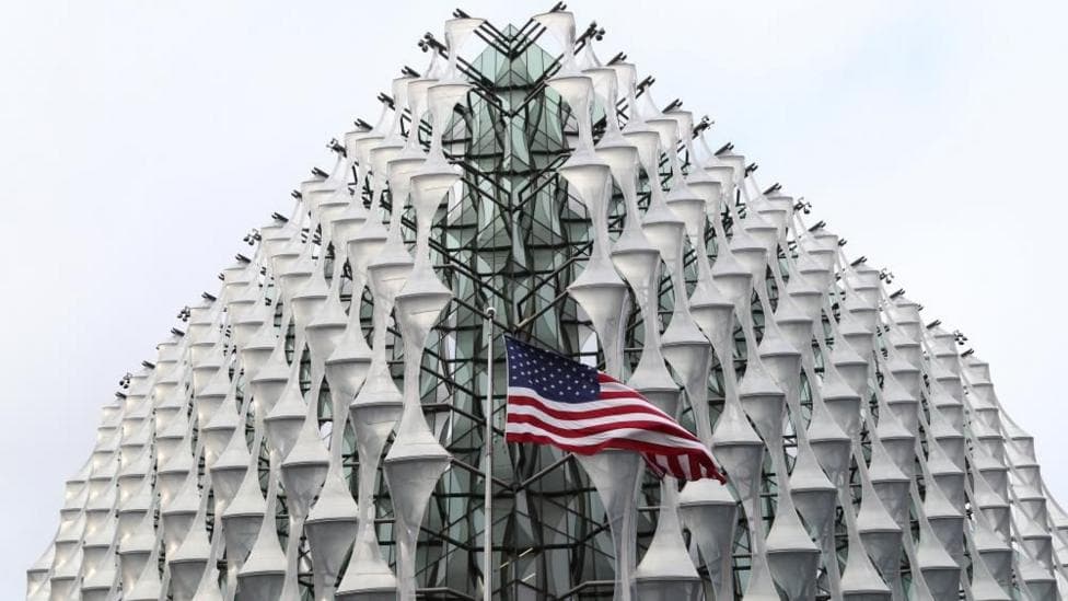 The exterior of the US Embassy in London with an American flag flying in front of the nearest corner, in the centre of the image.