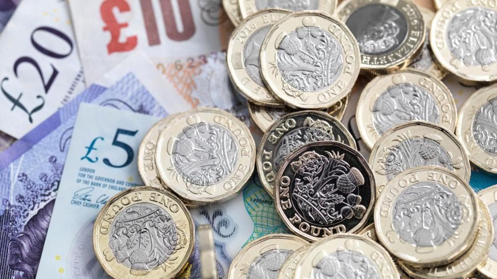 Gold coloured pound coins on a bed of sterling notes including £5 and £20 notes.