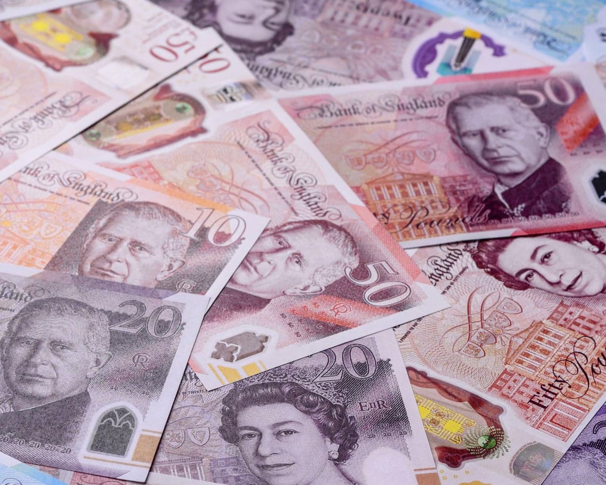 A pile of pound sterling cash banknotes, some featuring King Charles III, while others feature the late Queen Elizabeth II