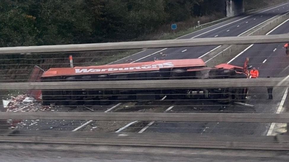 An overturned Warburtons lorry on the A1(M) near Bowburn, south of Durham. The orange lorry is sprawled across both lanes and there is a large amount of debris on the motorway.