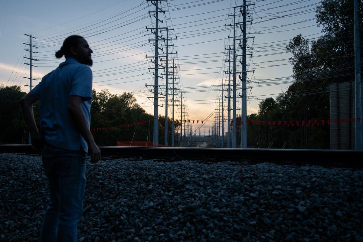 A man stands outside with many power lines overhead.