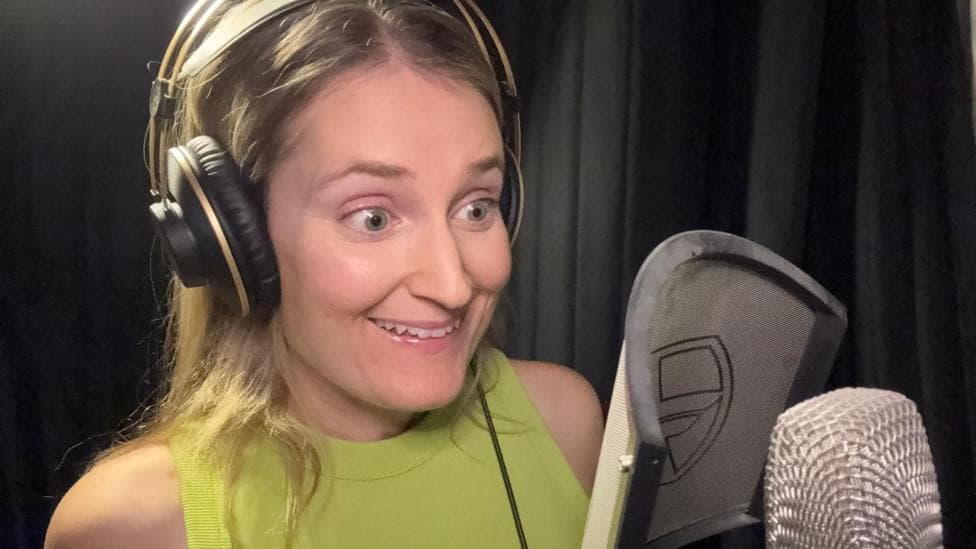 A woman with an enthusiastic facial expression wearing headphones and speaking into a microphone