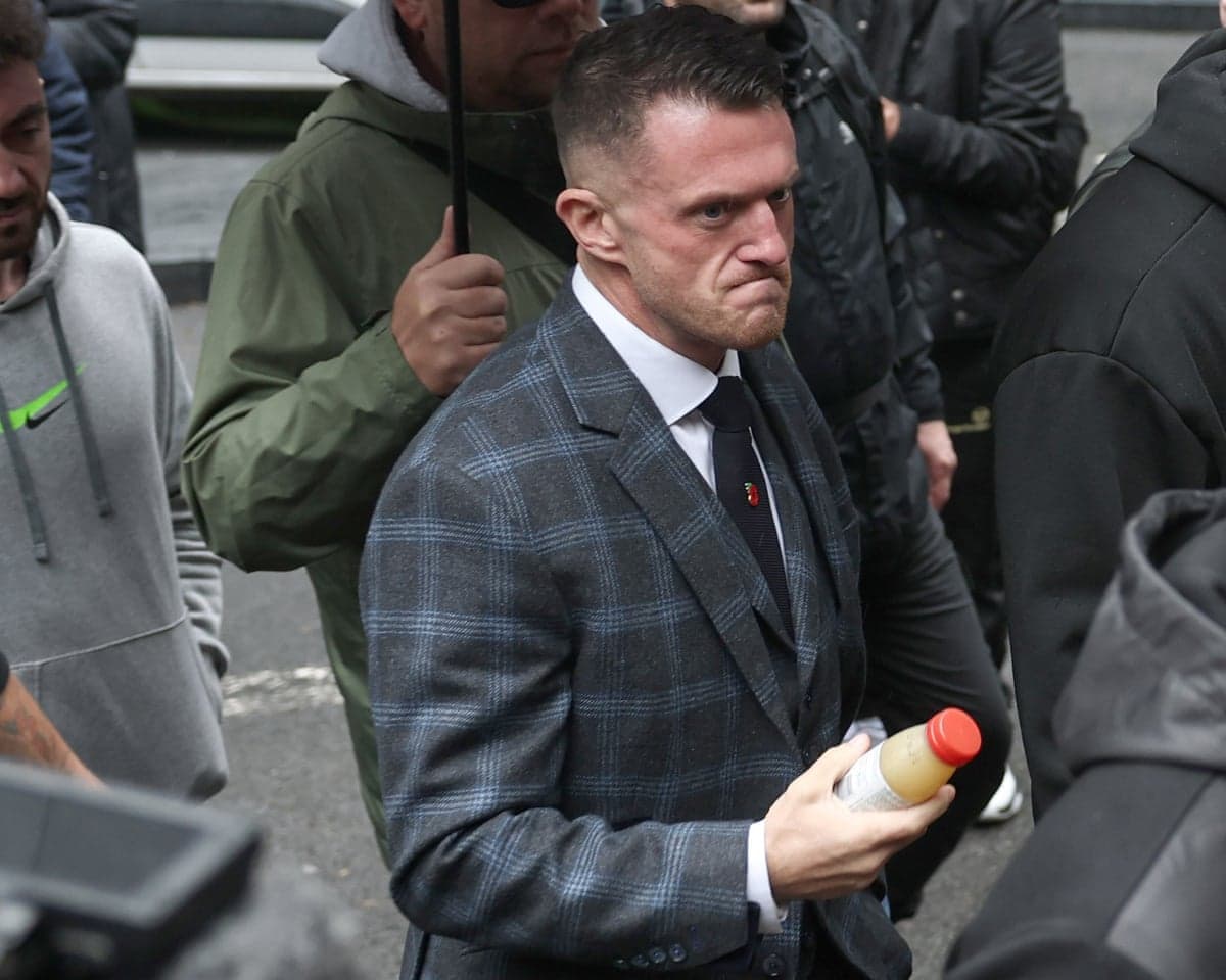 Tommy Robinson grimaces in a checked suit, holding a juice bottle, arriving at court