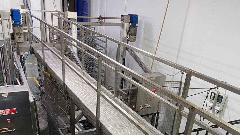Grey metal machinery, part of a production line with various metal guards and electrical boxes