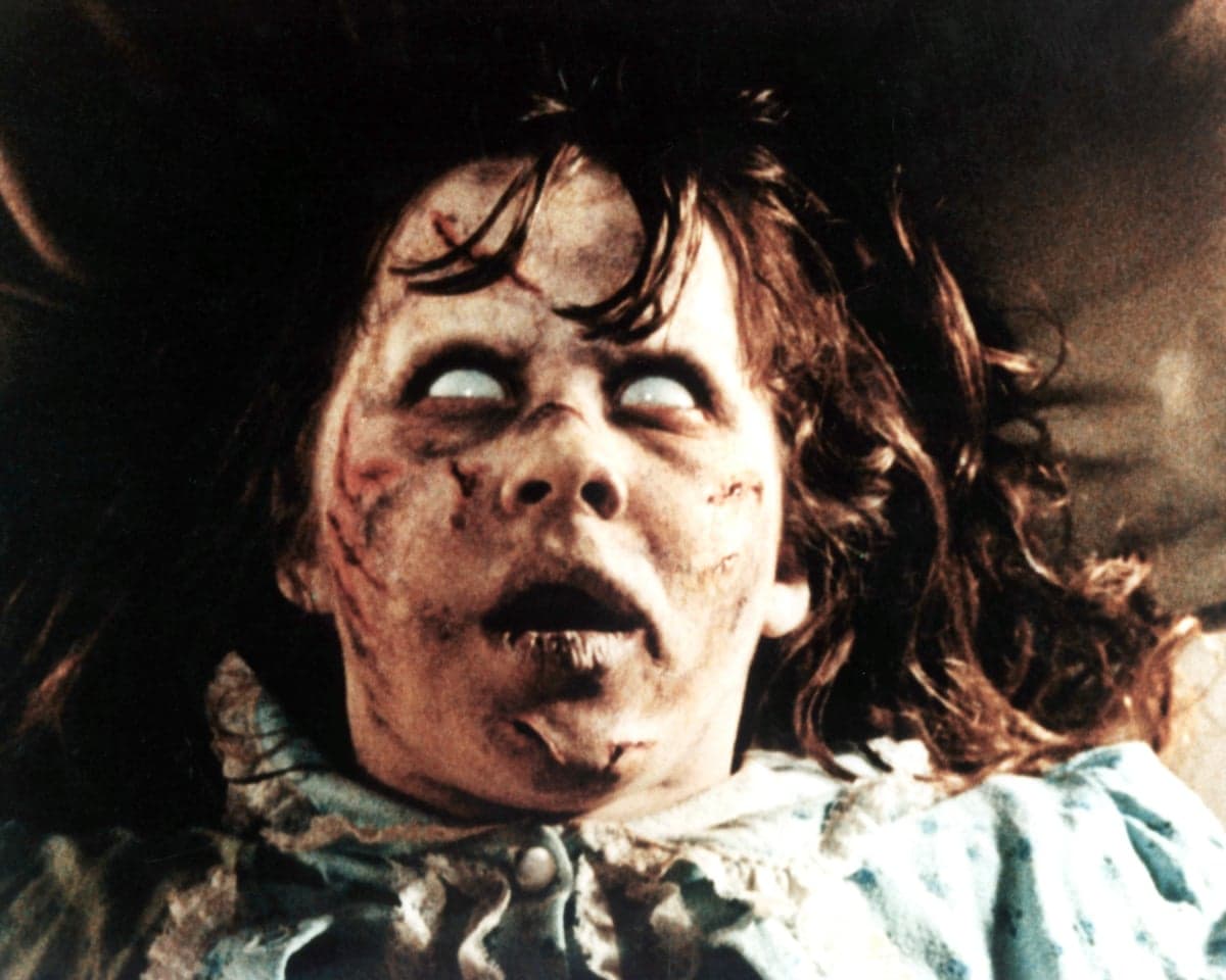 Regan, from The Exorcist, with pale scarred skin and white eyes, stares upward