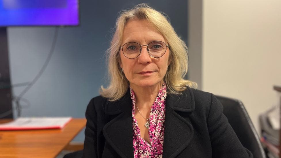 Elaine Millar is smartly dressed and sitting at a desk and looking at the camera.