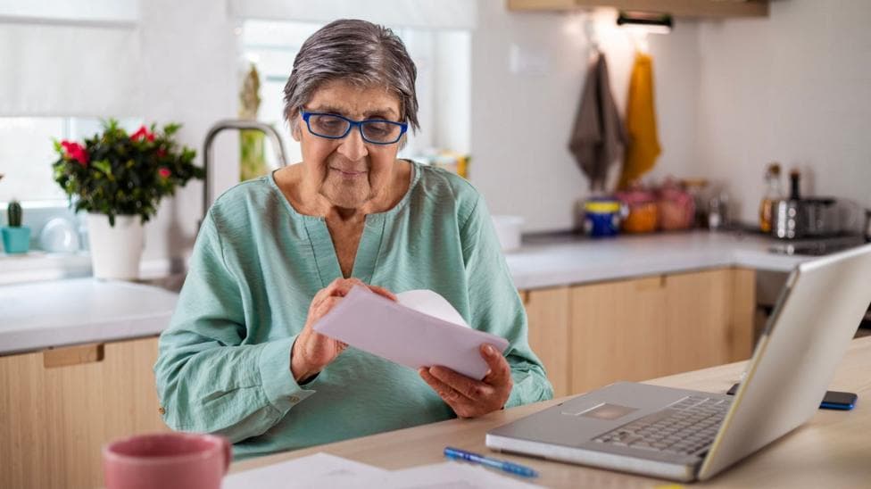A woman sitting in front of a laptop opens a letter.