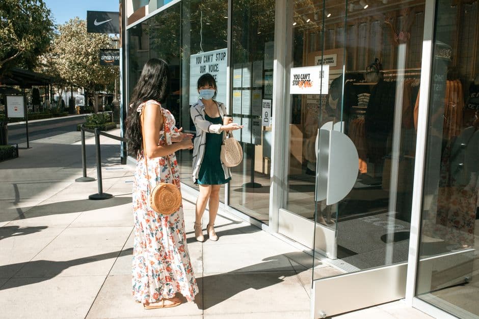 Two women social distancing outside a store during the daytime, highlighting shopping safety practices.