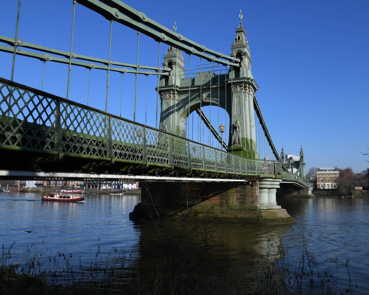 Hammersmith Bridge's green suspension towers span the River Thames under a clear sky