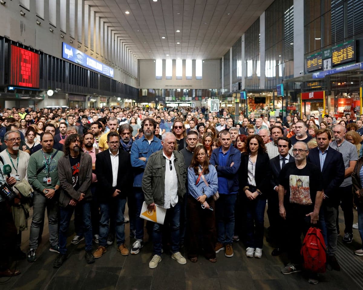 Crowd stands silently with heads bowed at Santa Justa station, mourning train crash victims